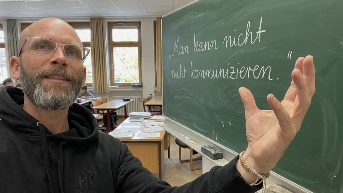 Sean Kollak im Klassenzimmer vor einer Kreidetafel mit dem Satz 'Man kann nicht nicht kommunizieren' – Watzlawicks Axiom als Ausgangspunkt für Meads Sprachtheorie und Arendts Zwei-in-einem