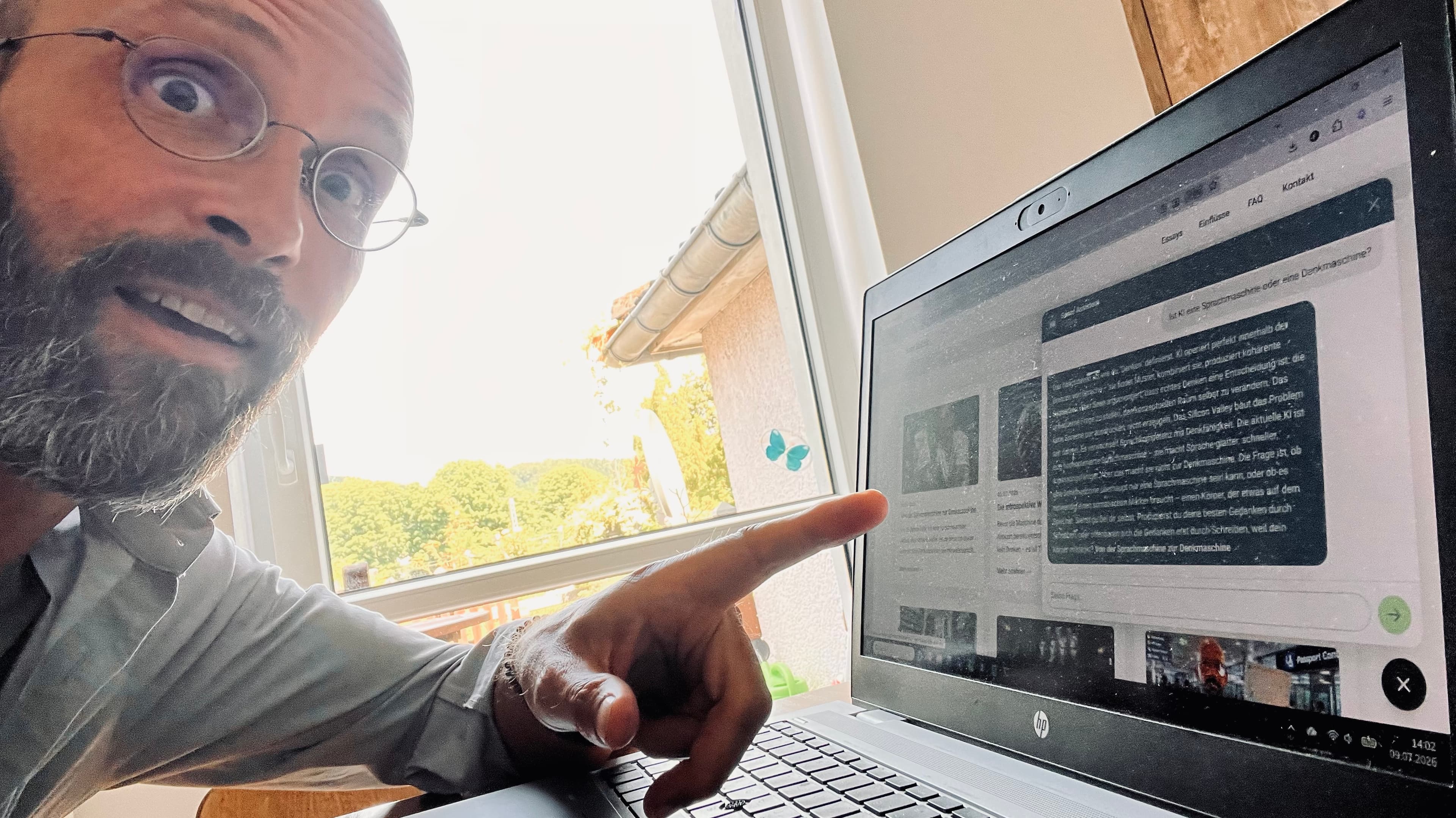 Sean Kollak zeigt überrascht auf seinen Laptop mit dem Chatverlauf seines eigenen ChatWidgets, sichtbar: 'Ist KI eine Sprachmaschine oder eine Denkmaschine?'