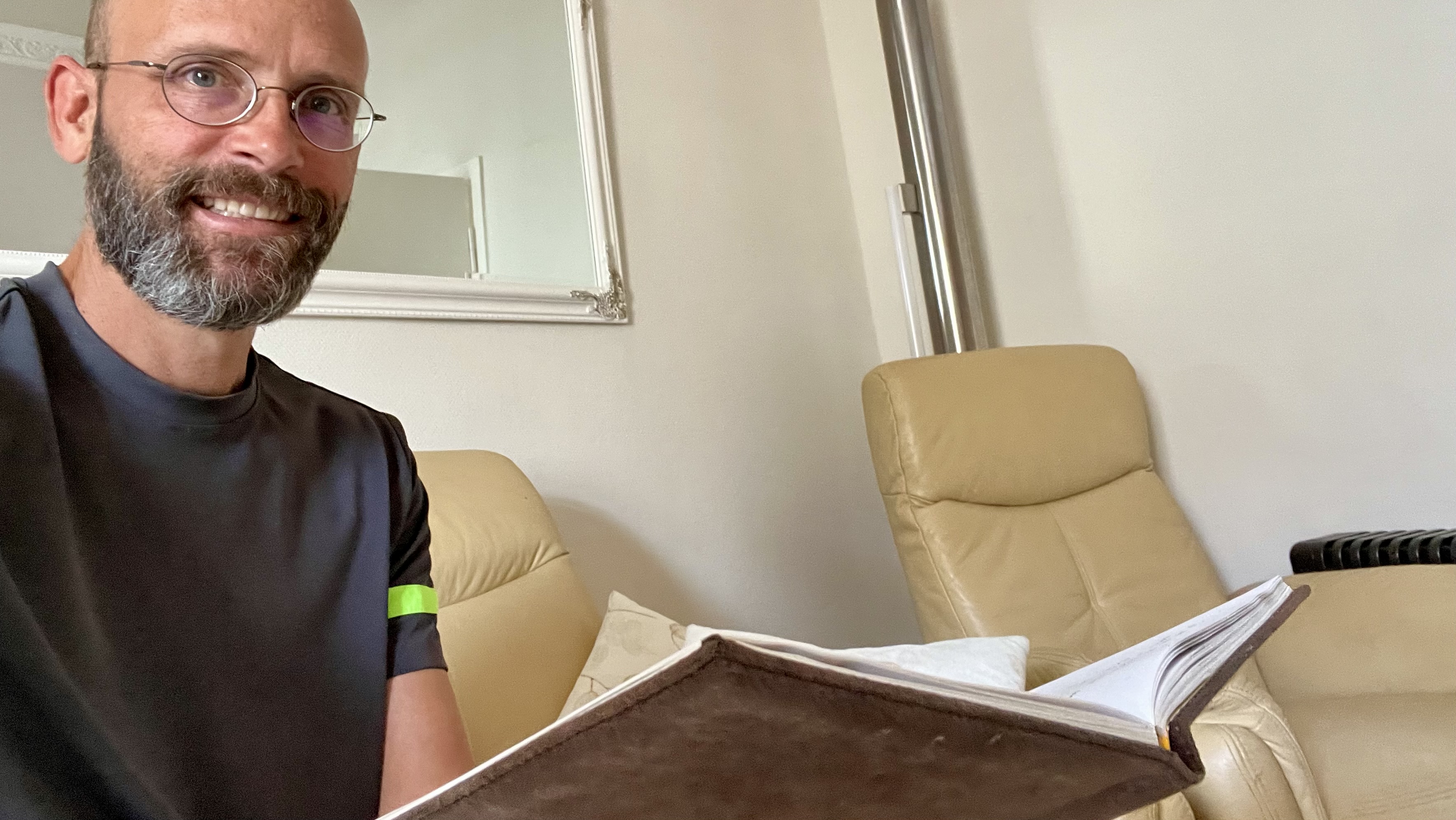 Sean Kollak lächelt mit einem aufgeschlagenen, ledergebundenen Notizbuch in der Hand – Ottos Notizbuch als Sinnbild für ein Werkzeug, das nie schmeichelt, weil es nichts will